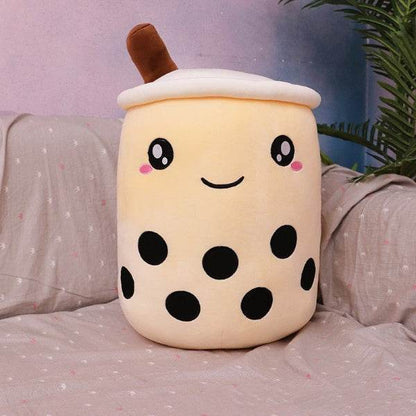 Cute plush toy resembling a bubble tea cup on a bed with a plant in the background
