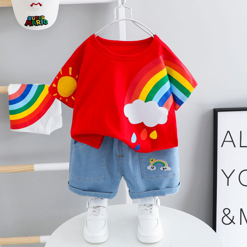 Children's outfit with red shirt featuring rainbow and sun design, blue shorts, and white sneakers on a gray background.
